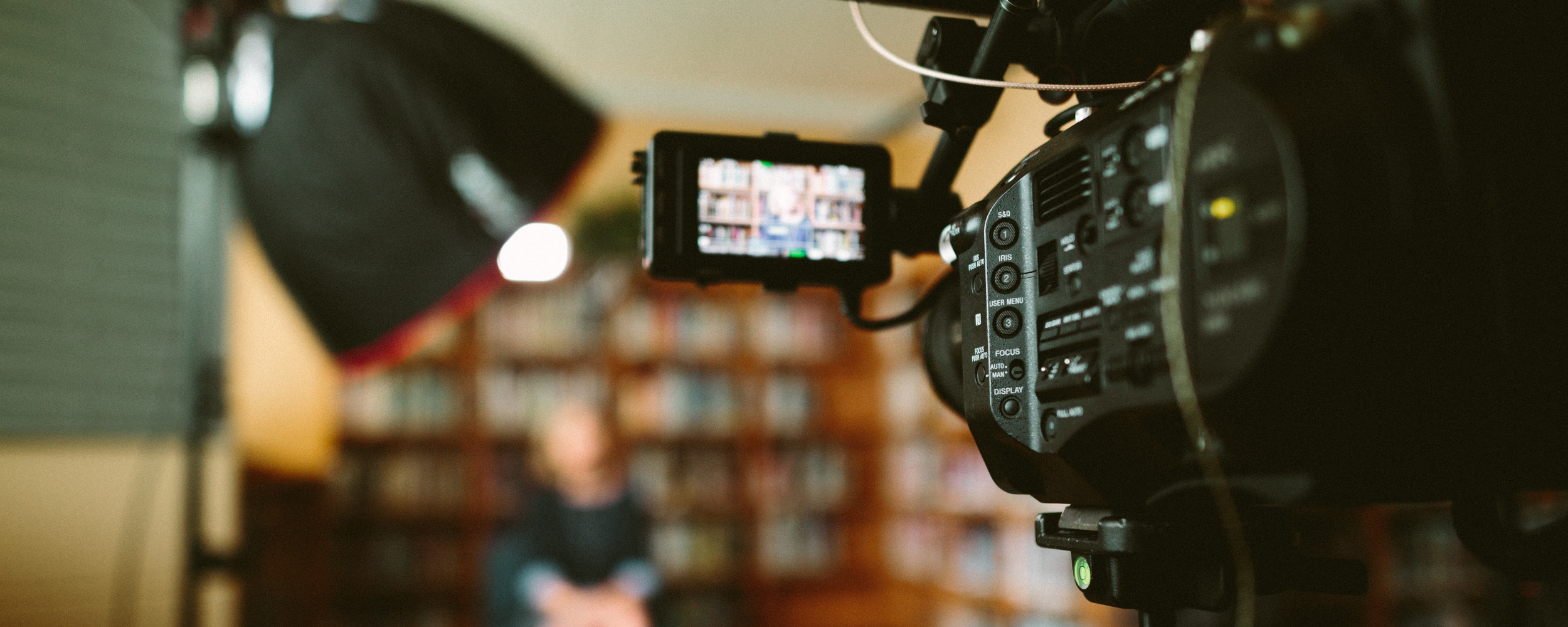 Perspektive eines Videografen neben einer Kamera, die auf eine Person vor einem Bücherregal gerichtet ist