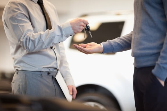 Man giving keys to another man in a car shop