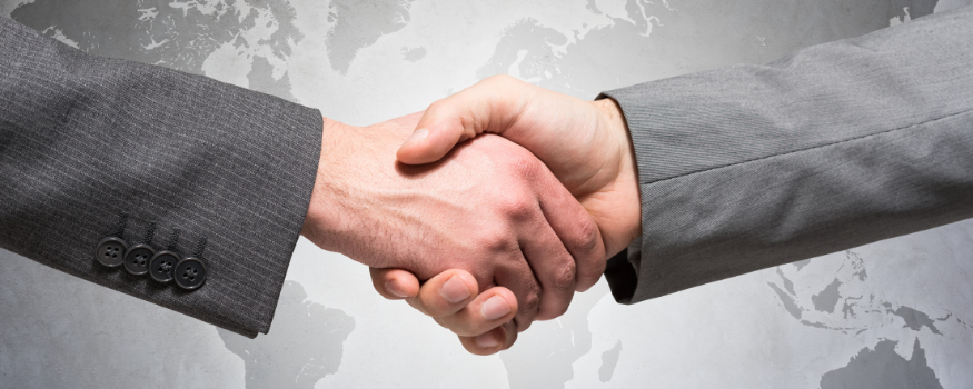 Zwei Geschäftsleute schütteln sich die Hand. Im Hintergrund eine Weltkarte